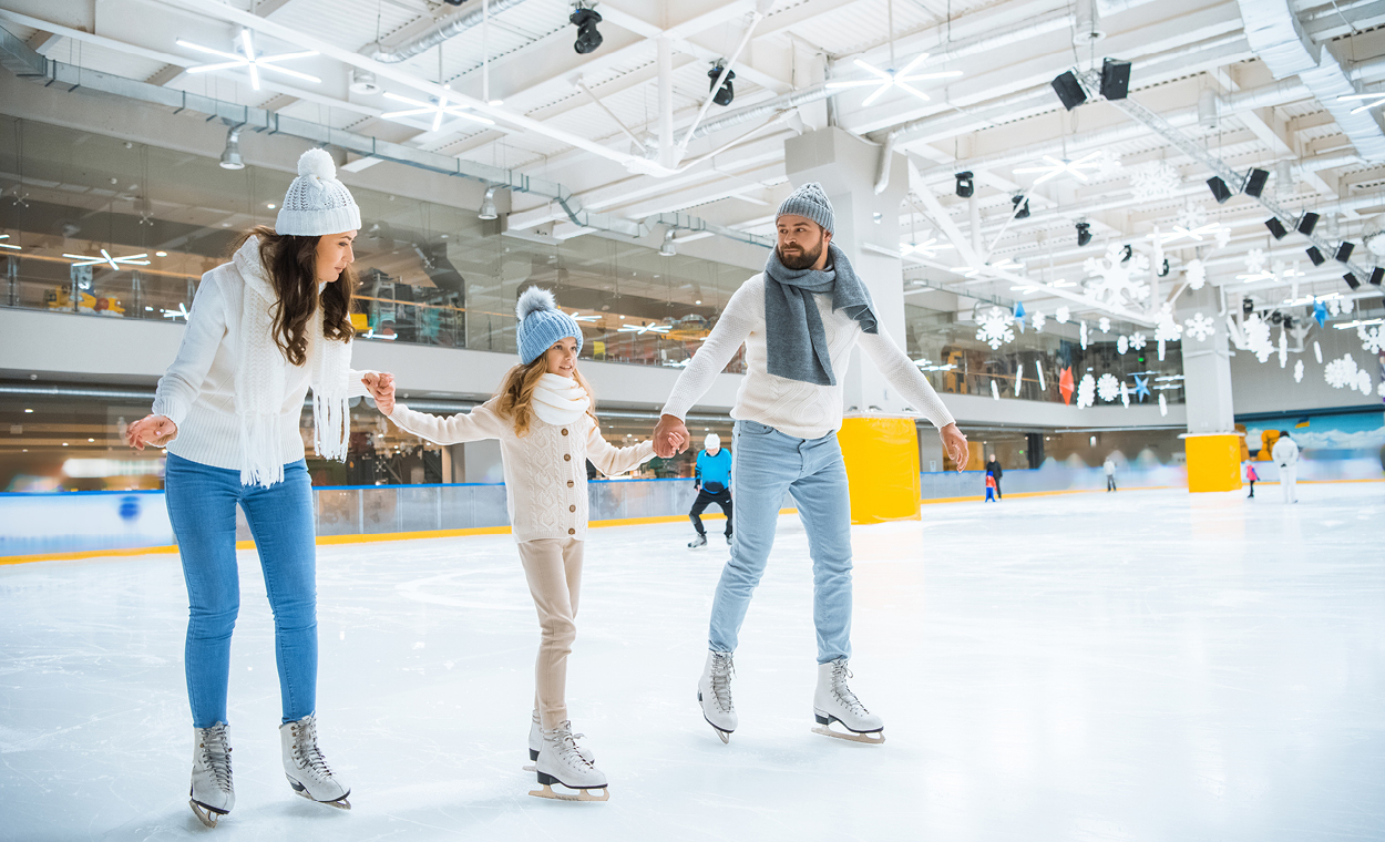 Two adults ice skating while holding a small childs hand trying to ice skate between them.