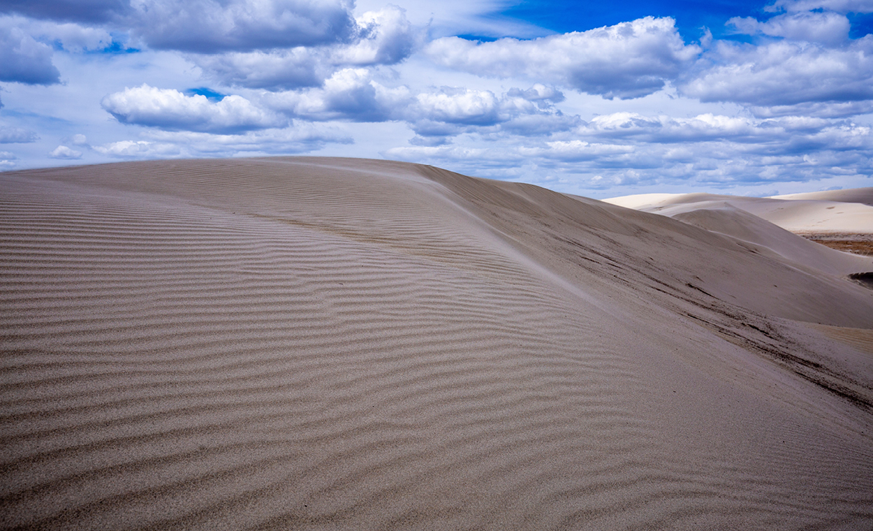 Sand dune with wispy clouds in the bright blue sky.