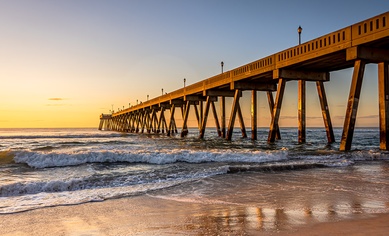 A long pier jutting over the ocean under a sunset.