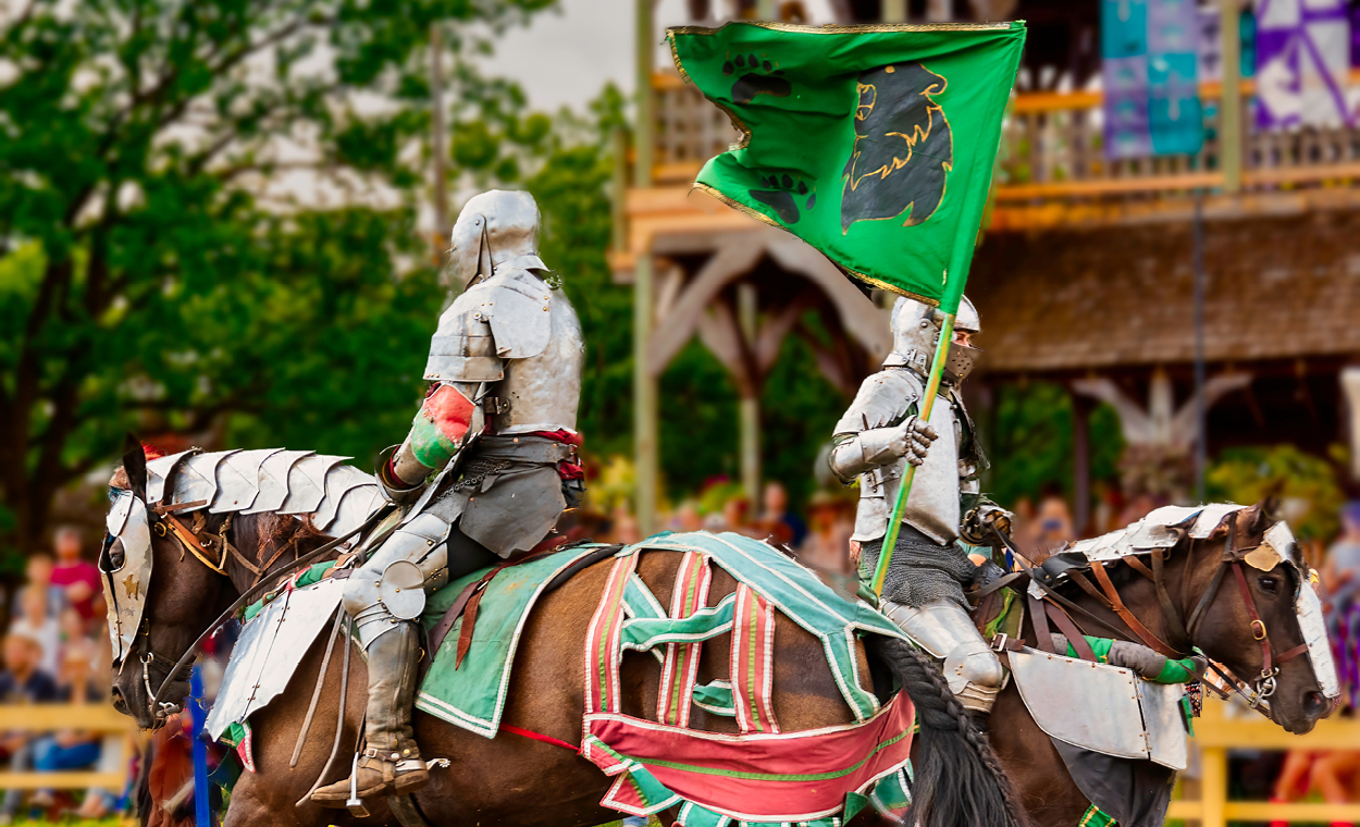 Two metal knights sitting on a armored horses with joust poles in the air.