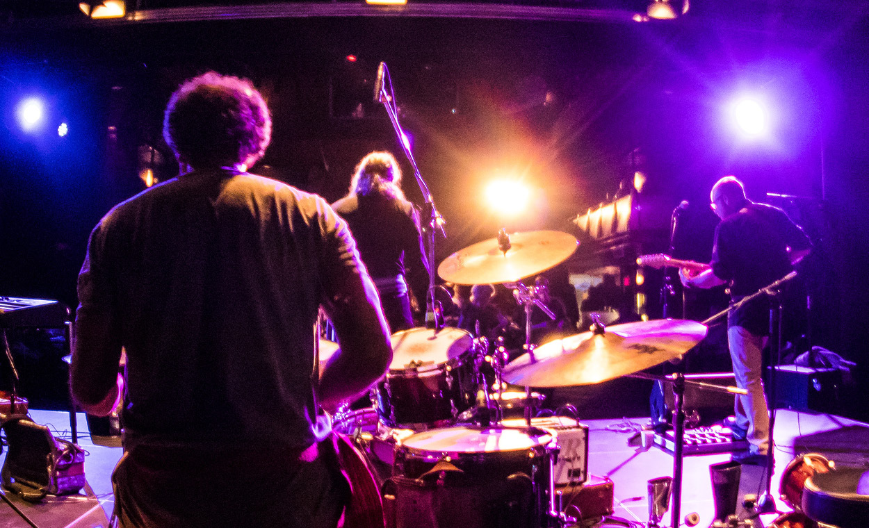 Band set up on stage with view of bright purple and blue lights shining on them.