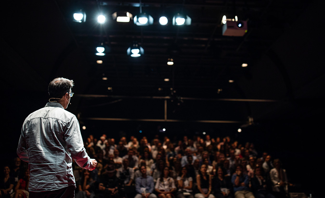 Dimly lit audience watching a person on stage.