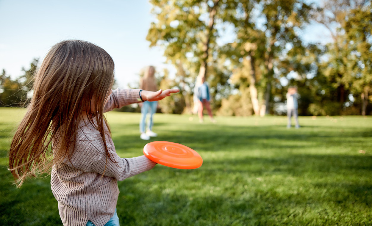 Adults and children throwing a Frisbee in a park.