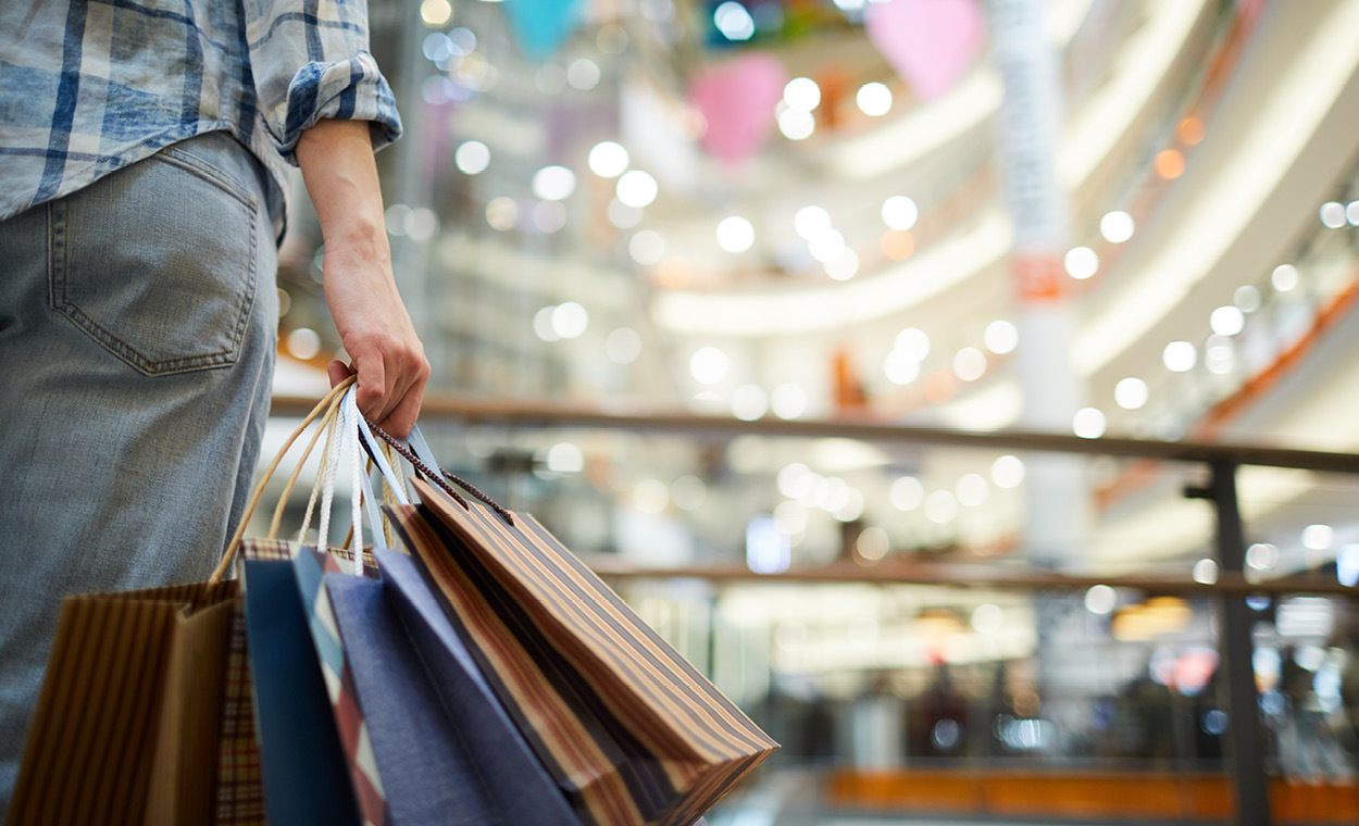 Hand holding multiple shipping bags in the center of a shopping mall.