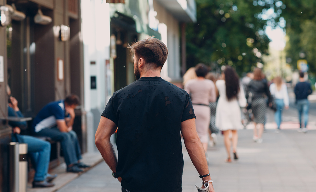 Man walking down a sidewalk next to multiple storefronts.