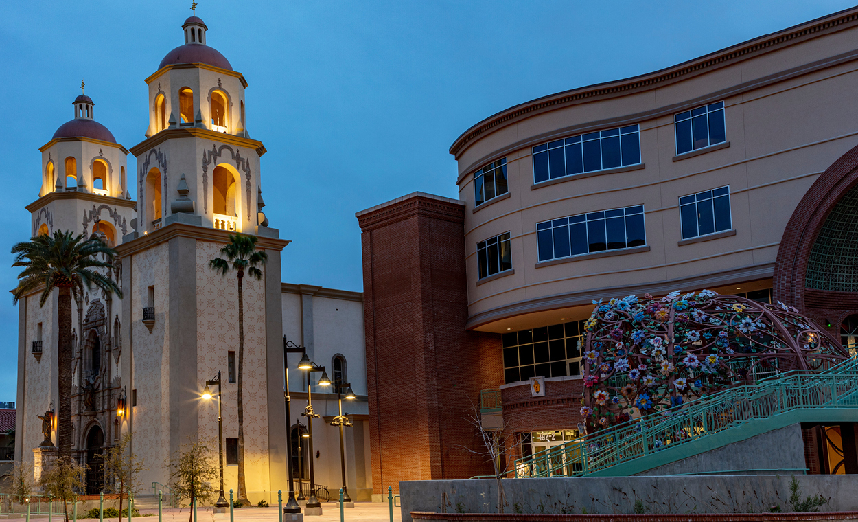 Large southwestern style church next to a building with a sculpture out front.