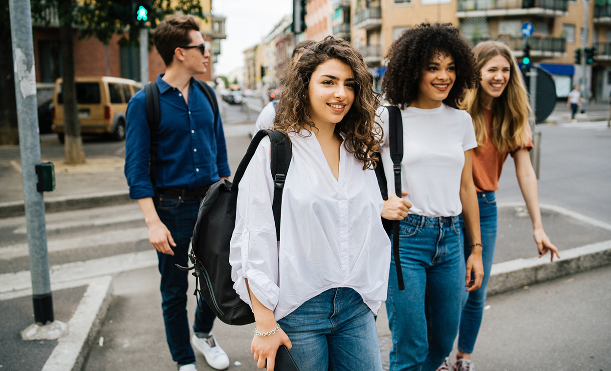 Multiple people walking across a street in a metropolitan area.