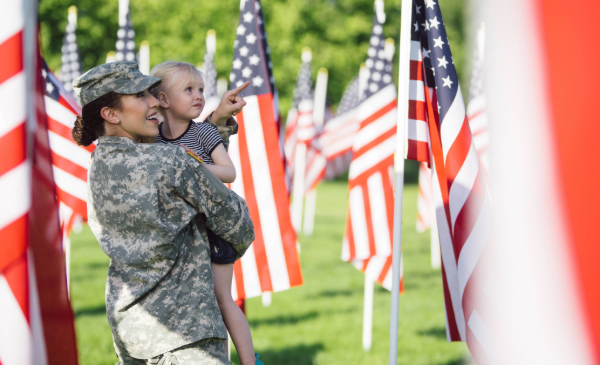 A woman holds a young child while surrounded by American flags in a grassy area.