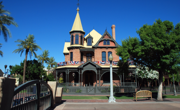 A tall, Victorian-style house sets between trees under a clear, blue sky.
