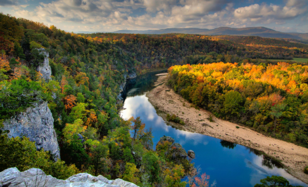 A river winds between rock formations and trees under a cloudy sky.