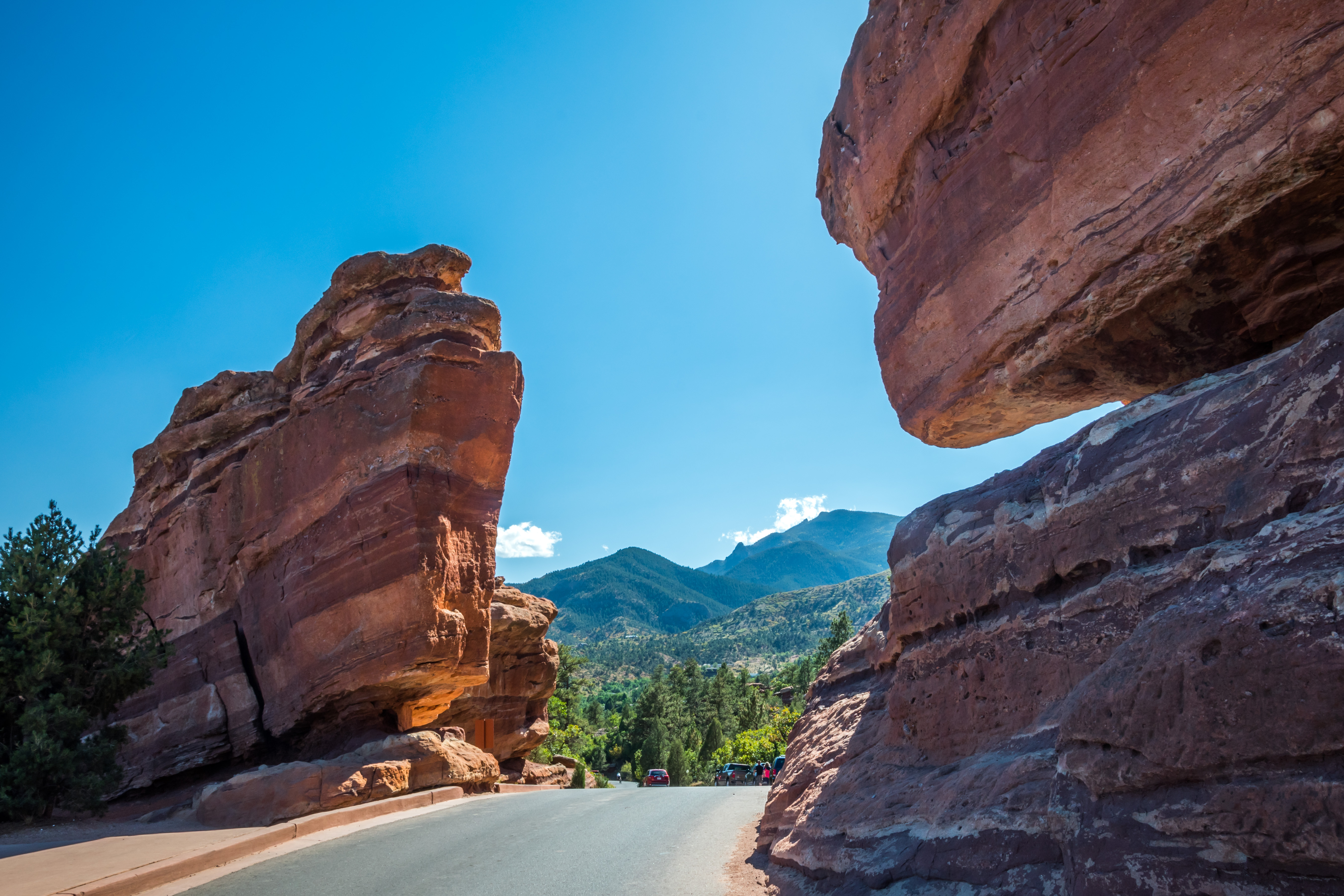 Two large, red rock formations flank a paved road with hills in the distance, all under a clear blue sky.