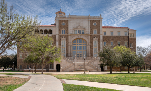 An old, brick school sets below a cloudy blue sky.
