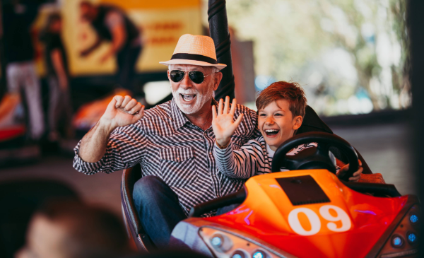 An adult and child smile and wave while riding in a bumper car.