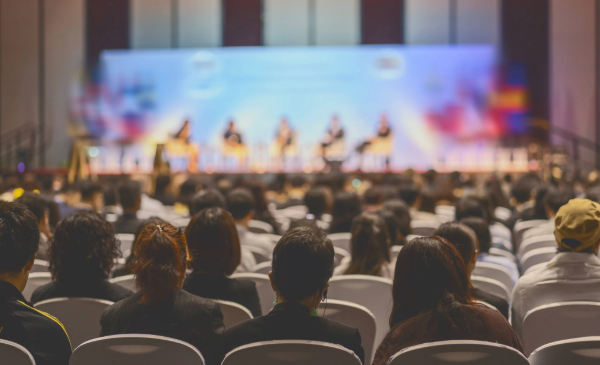A group of people watch a presentation on a lit stage.