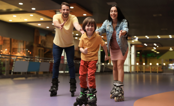 A young boy on roller skates is closely followed by his parents as they reach out to him.