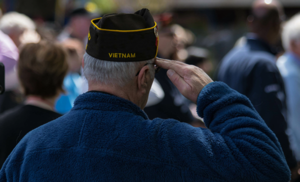 A man facing away from the camera wears a Vietnam military-style hat while saluting.