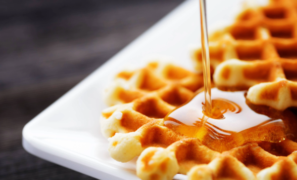 Syrup is poured over two waffles that sit on a white, square plate.