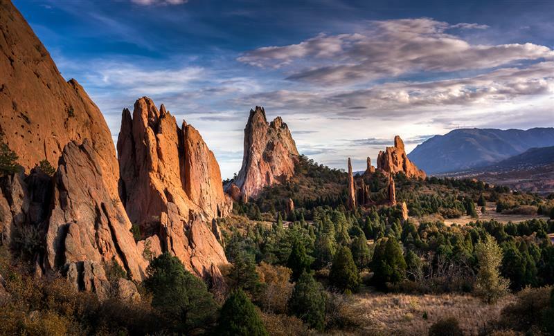 Landscape of large jagged rocks towering above sparse trees and mountains.