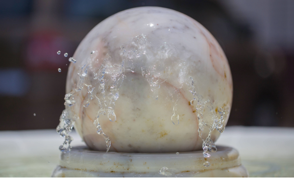 A large white, marble ball sits on top of a marble pedestal with water.