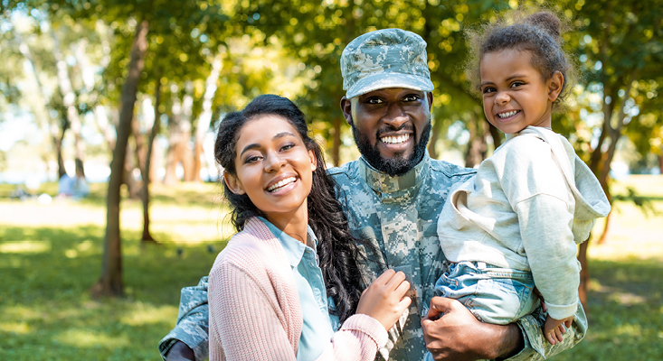 Man in a military in uniform in park with wife and child.