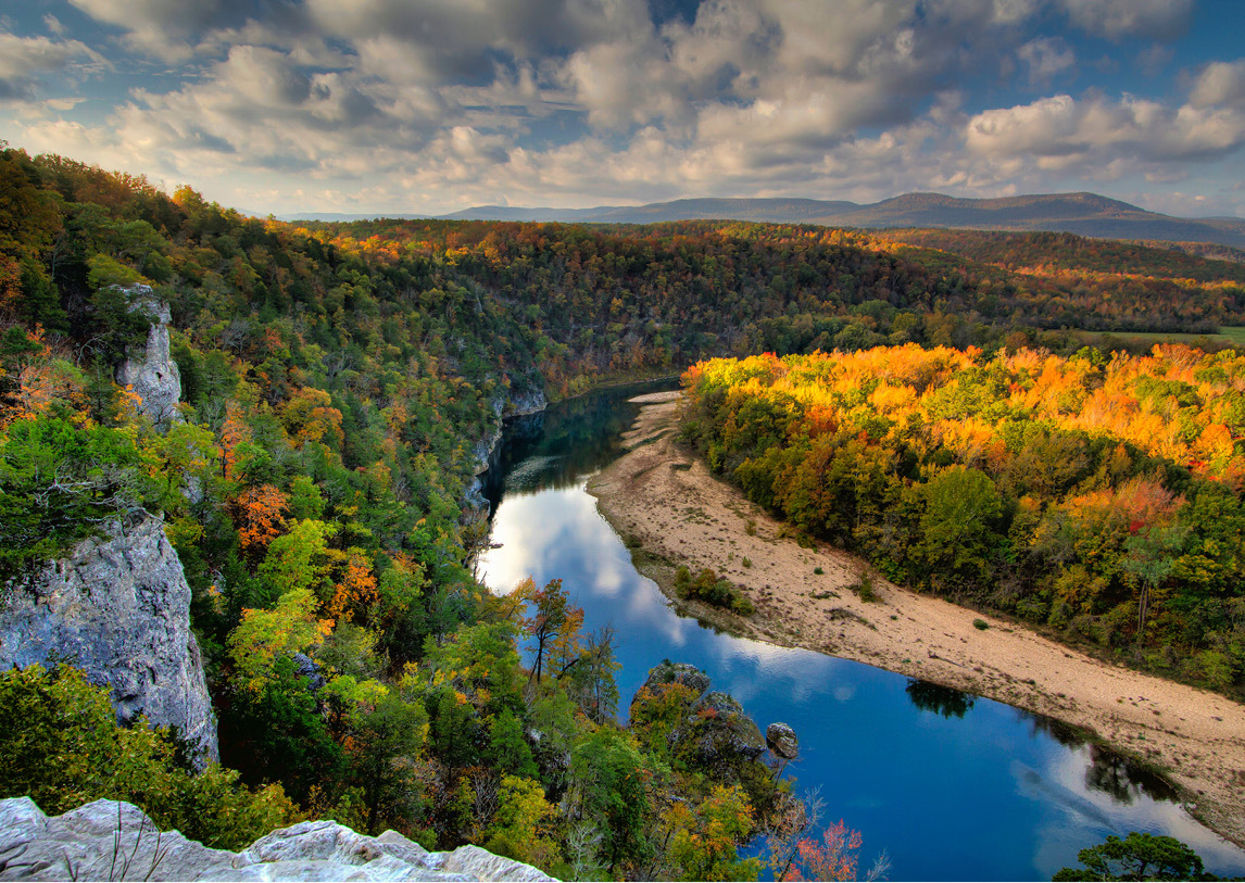 Green and yellow trees surrounding a winding glass river.