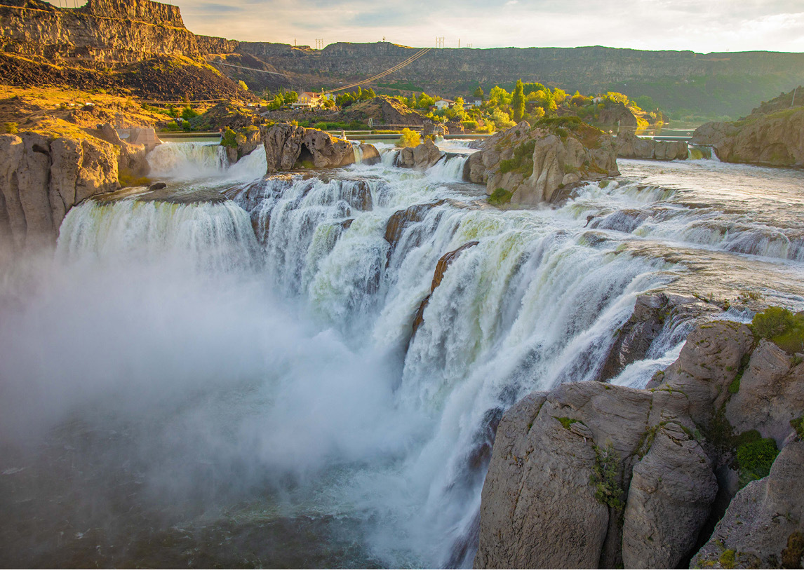 An aerial view of a tall, wide waterfall nestled between natural rock formations under a cloudy sky.