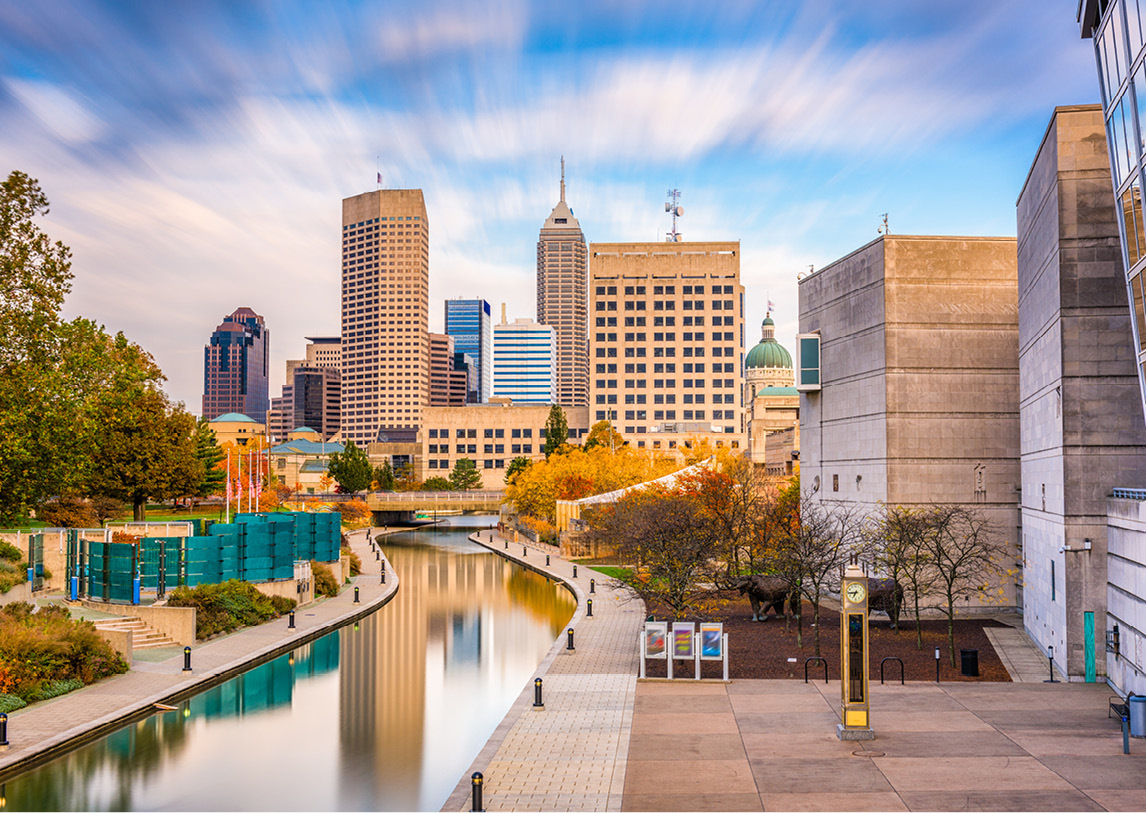 A downtown area sits next to a curved, man-made river under a partly cloudy sky.