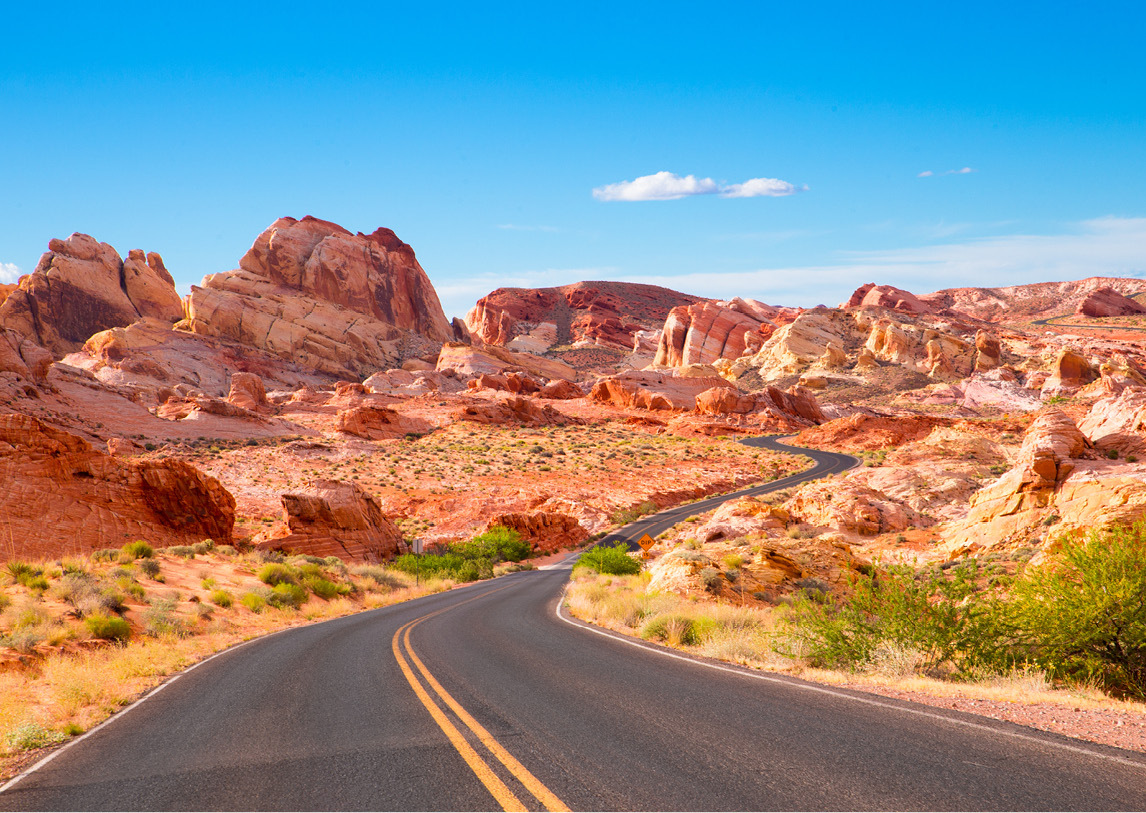 A winding, paved road twists up through natural rock formations under a bright blue sky.