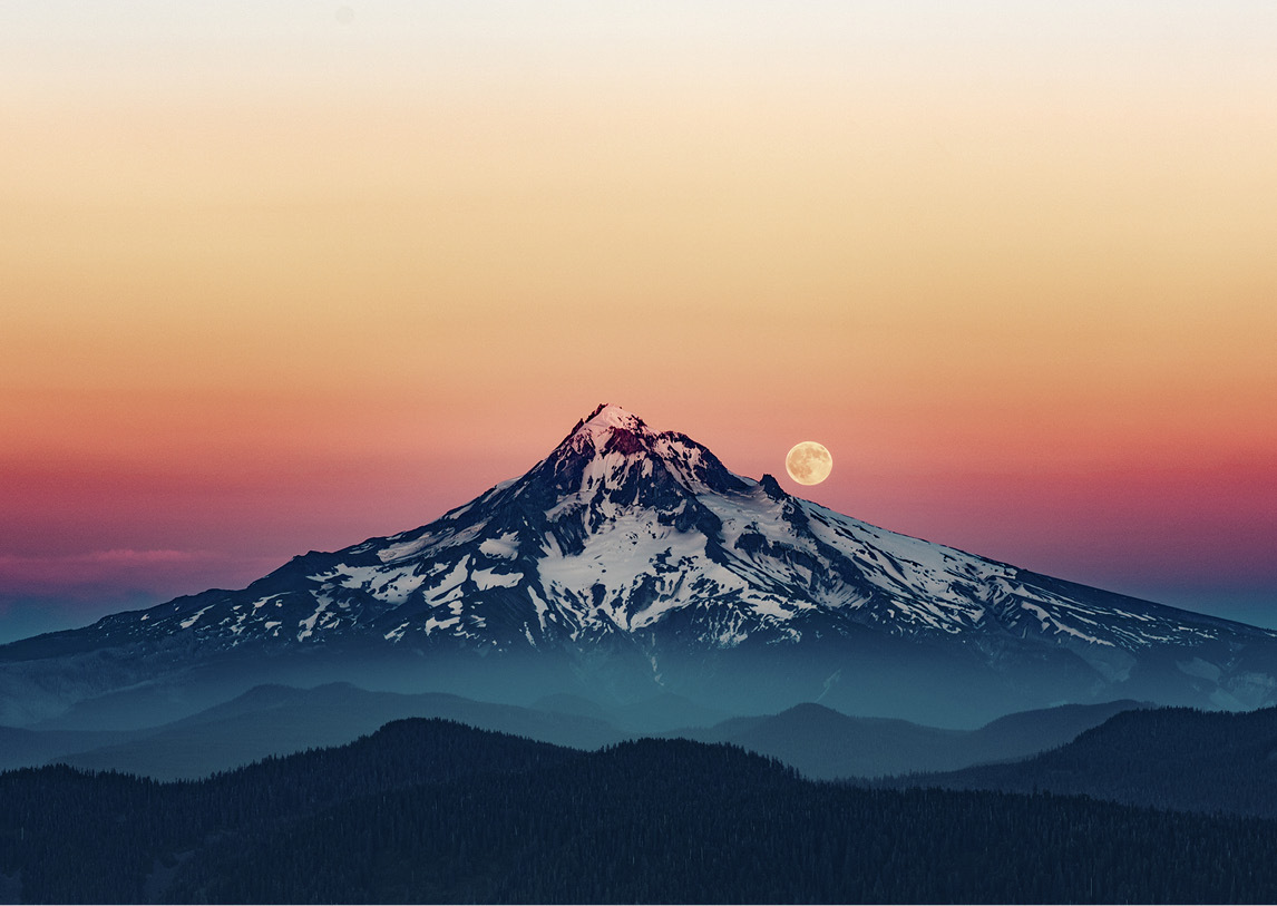 A lone, snowy mountain rises above fog with a full moon peaking from behind, under a blue, red, and orange sunset.