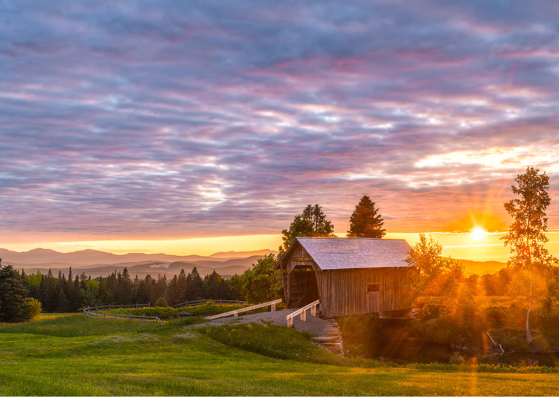 Grassy farm with small brown shack and a blue, orange, and yellow sunset.