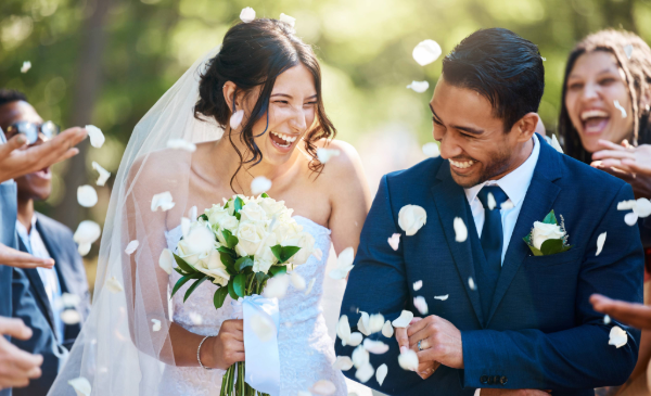A bride and groom smile as guests throw white flowers at them following a wedding.