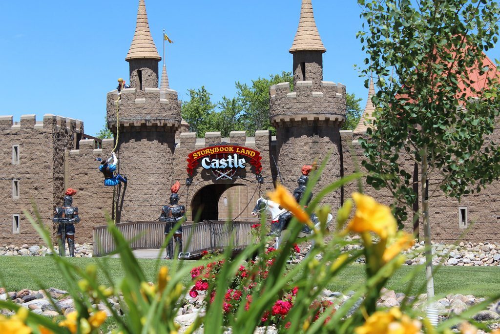 Brown castle structure with a drawbridge entrance and two towers on either side. Above the entrance there is a sign that states "Storybook land castle." The front of the image is slightly obscured by a bundle of yellow flowers.