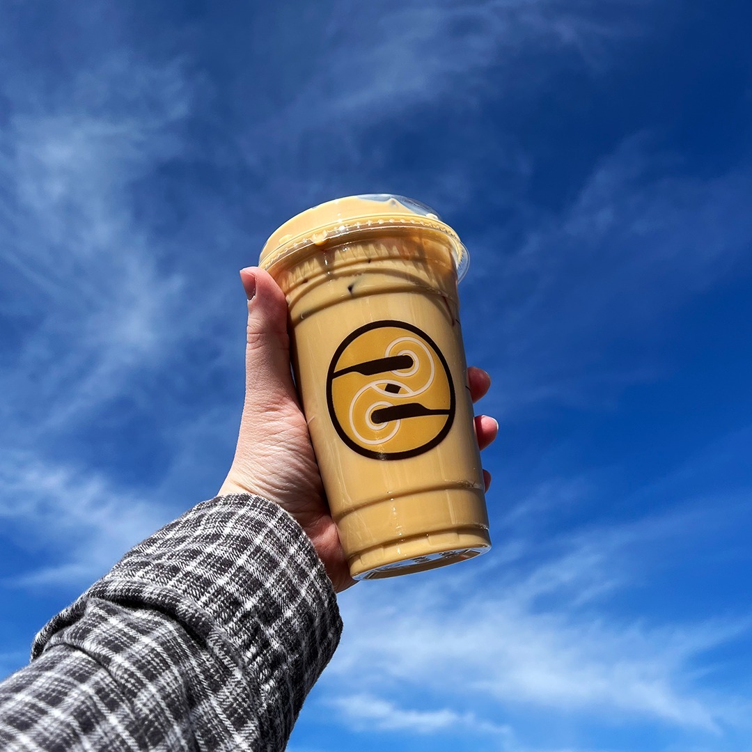 Hand holding an iced coffee with a blue sky background.