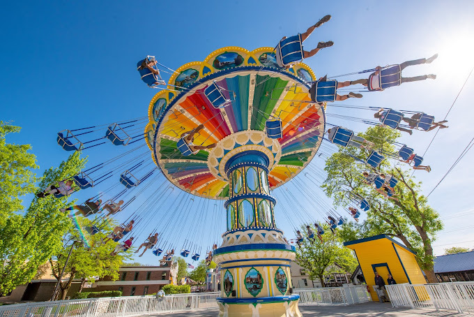 Rainbow colored circular amusement park ride with multiple people in the seats.