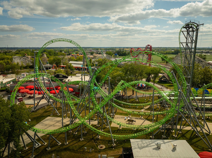 Green rollercoaster surrounded by trees and other amusement park rides.