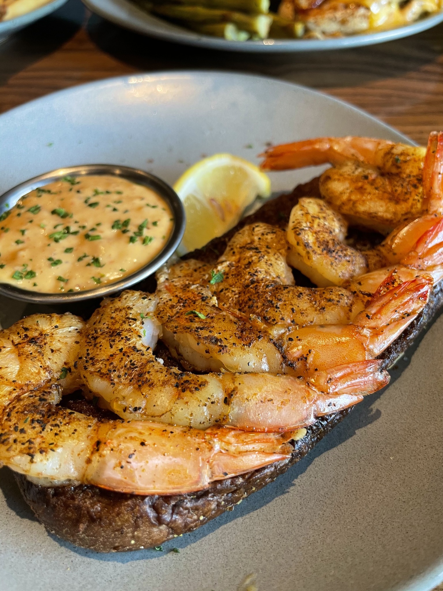 Close view of seasoned shrimp and a cup of sauce on a blue plate.
