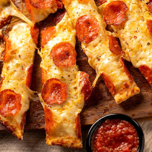 Pizza breadsticks with pepperoni and cheese. A small black cup with marinara sauce is set off to the side.