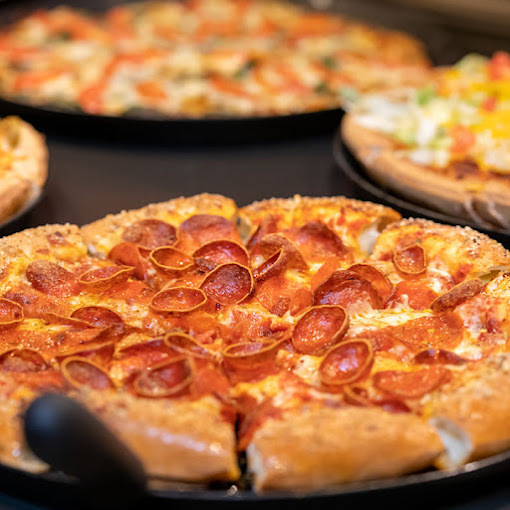 Close view of a fluffy pizza with pepperoni. In the background there are three other pizzas.