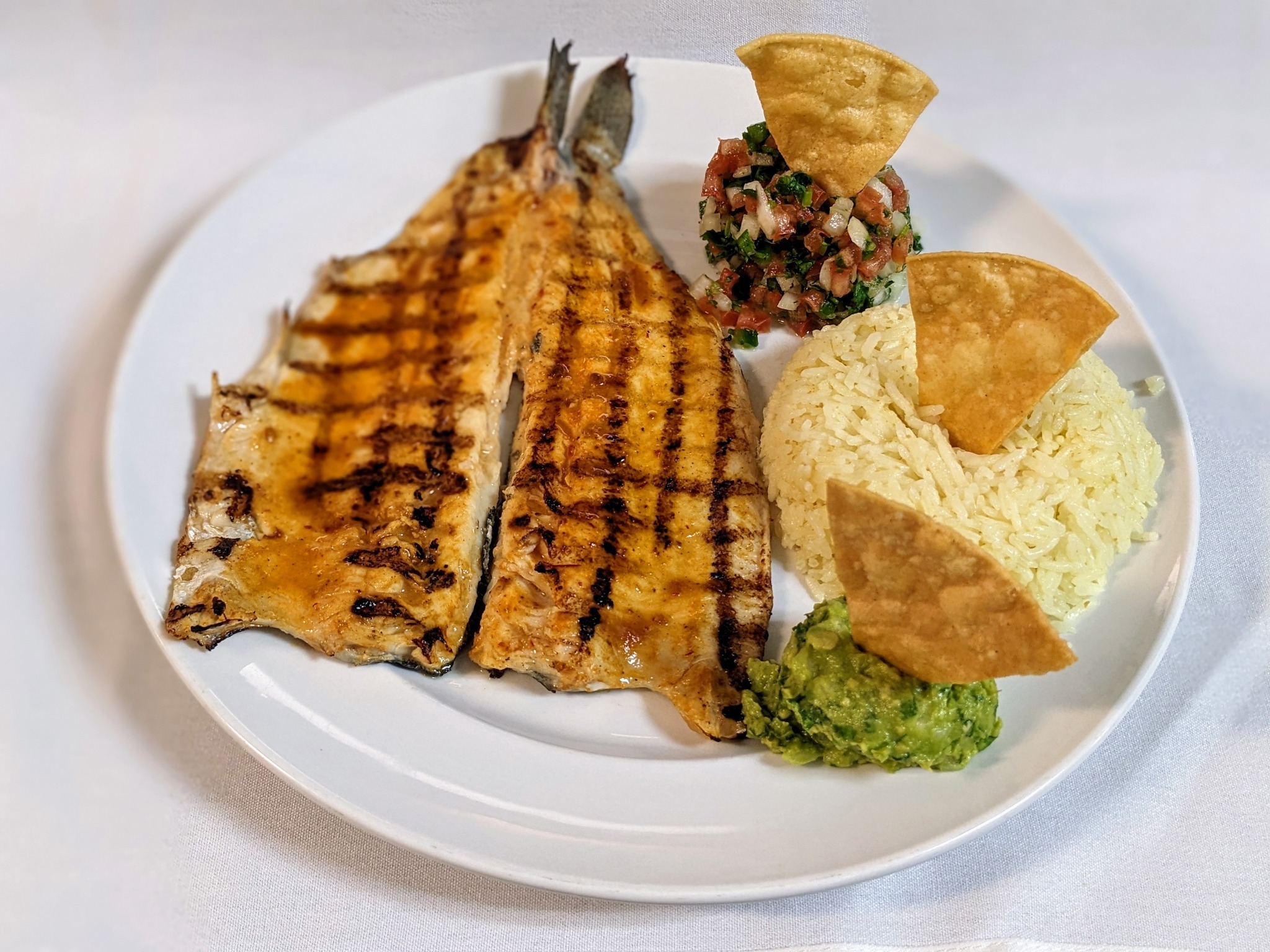 Grilled fish, rice, guacamole, and salsa on a white plate. All items, excluding the fish, have a triangular chip sticking out of it.