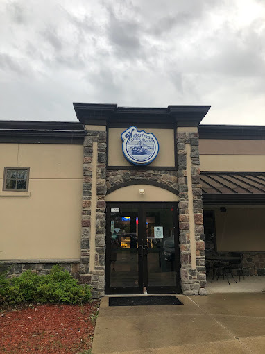 Exterior view of a grey building during a cloudy day. The glass doors have built-in brick columns on either side. The sign above the door is circular and blue.