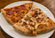 Three large pizza slices, one pepperoni and one specialty meat pizza, served on a white plate over a wooden table.
