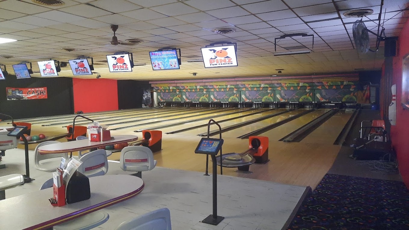 A view of bowling lanes, with tv's overhead and a red accent wall to the left and right.