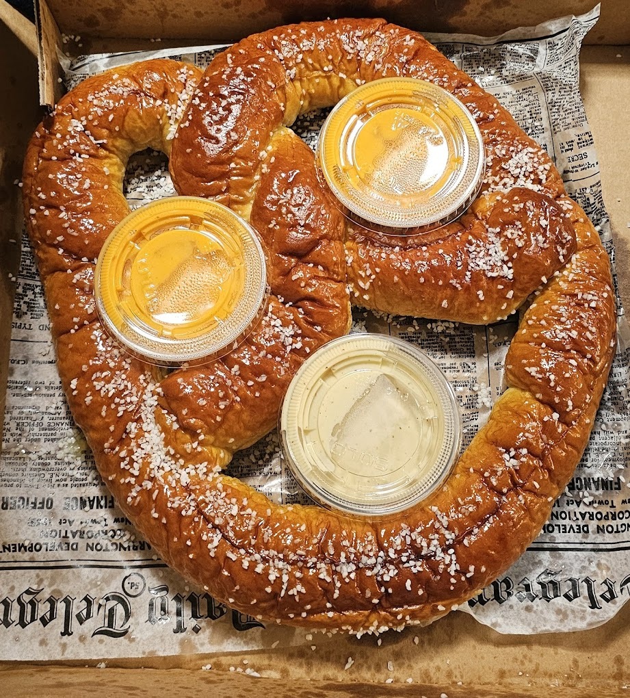 A large soft baked pretzel on paper with three sides of cheese.