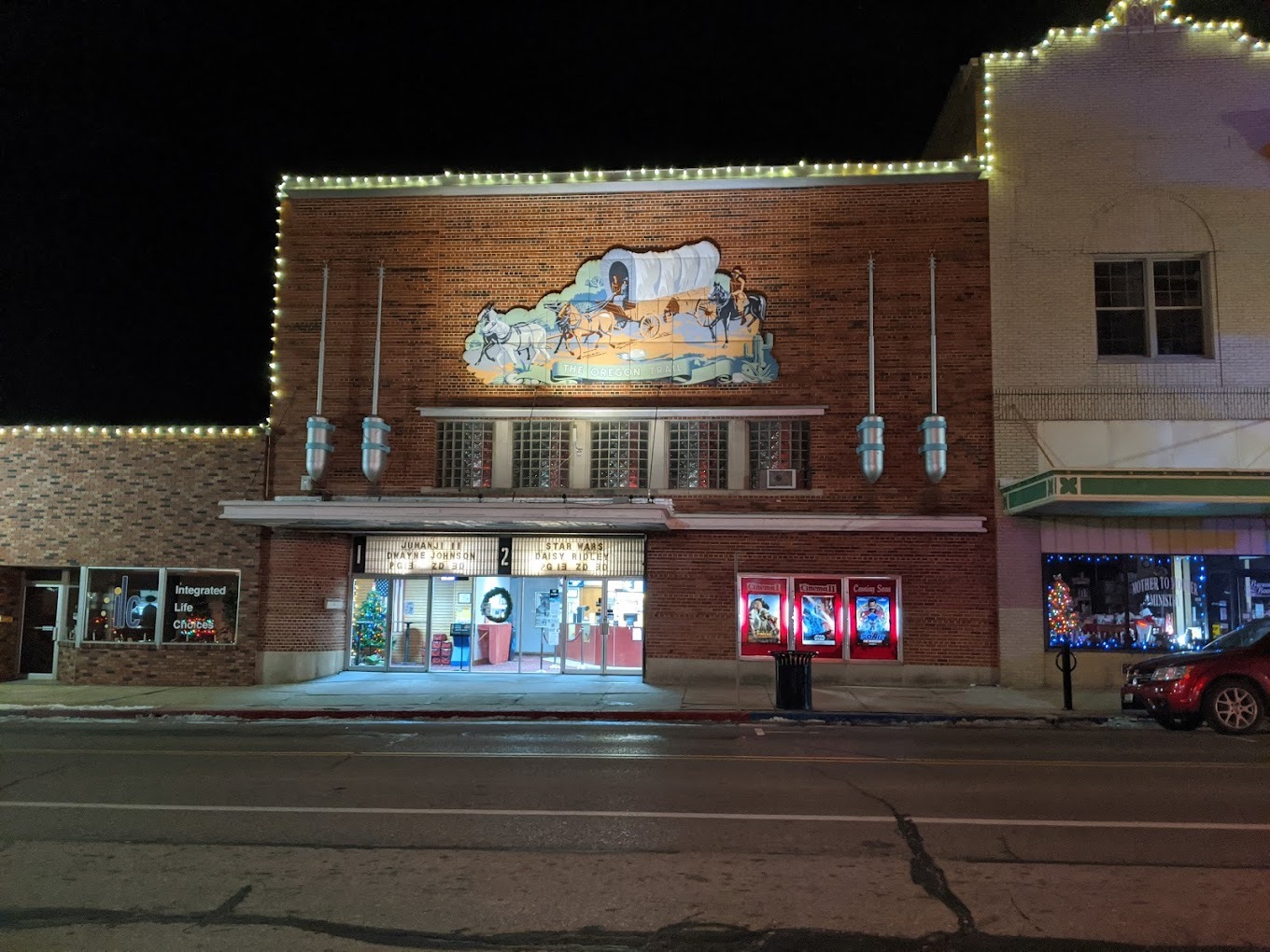 An outside view of another part of a theater, a brick building with a large sign overhead the door, depicting a horse and wagon.