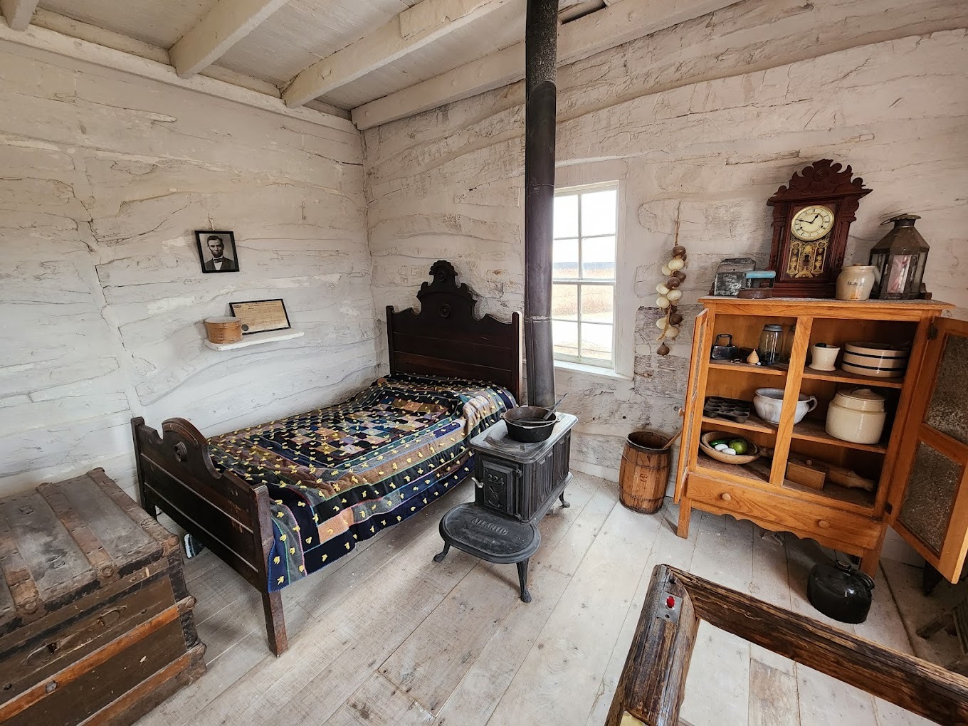 A small room full of old furniture, an antique furnance in the middle of the room, and old knick-knacks.
