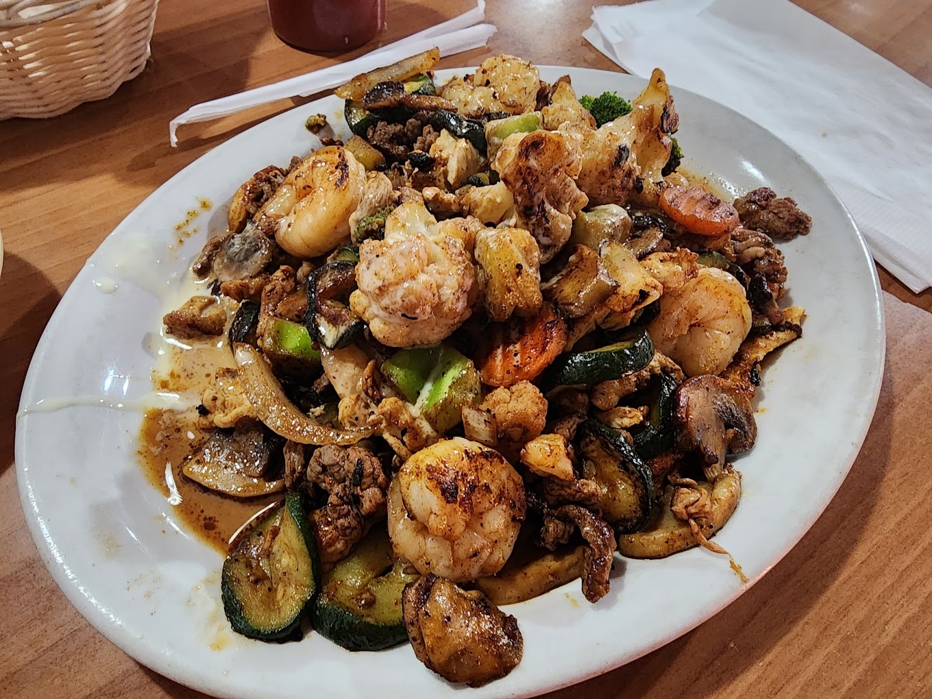 A white plate full of a shrimp dish grilled with cucumbers, shrimp, tomato and onion.