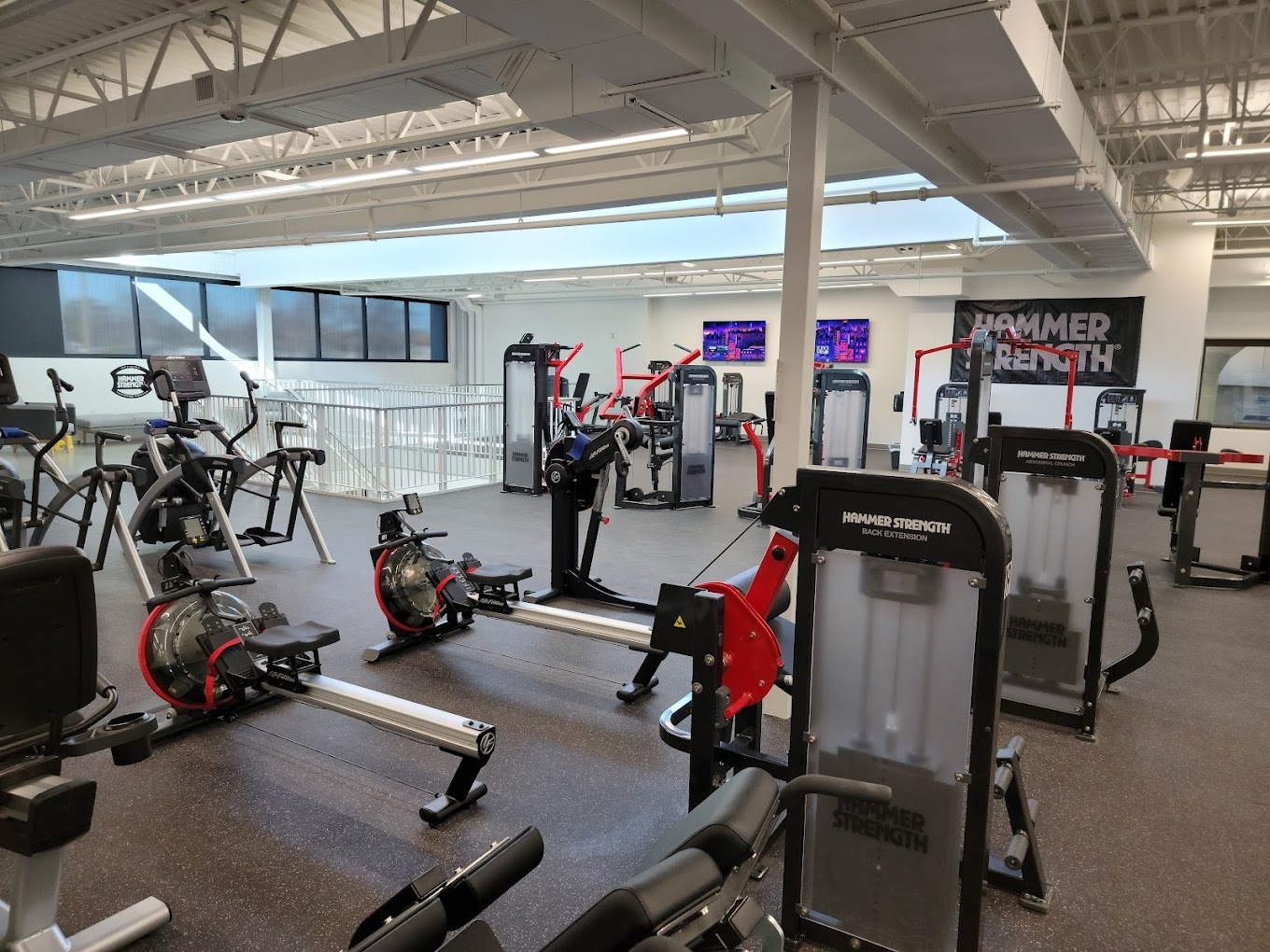 A room full of strength and cardio equipment, TV's on the walls and sky lights in the ceiling.