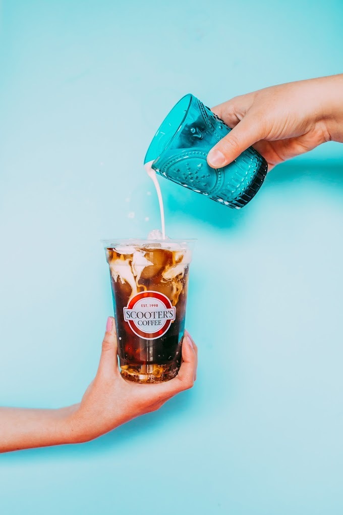 A iced coffee being filled up with cream from a blue cup.