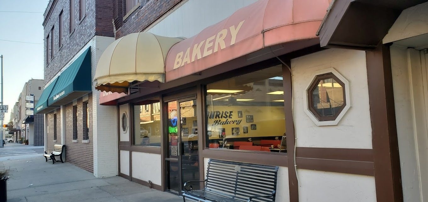 An outside view of a bakery with red and yellow awnings over the windows and doors. A red awning reads "Bakery" in yellow lettering.