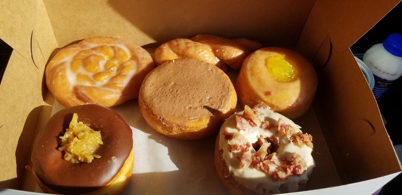 A box full of various kinds of donuts, a mix of plain glazed and chocolate covered donuts topped with nuts.